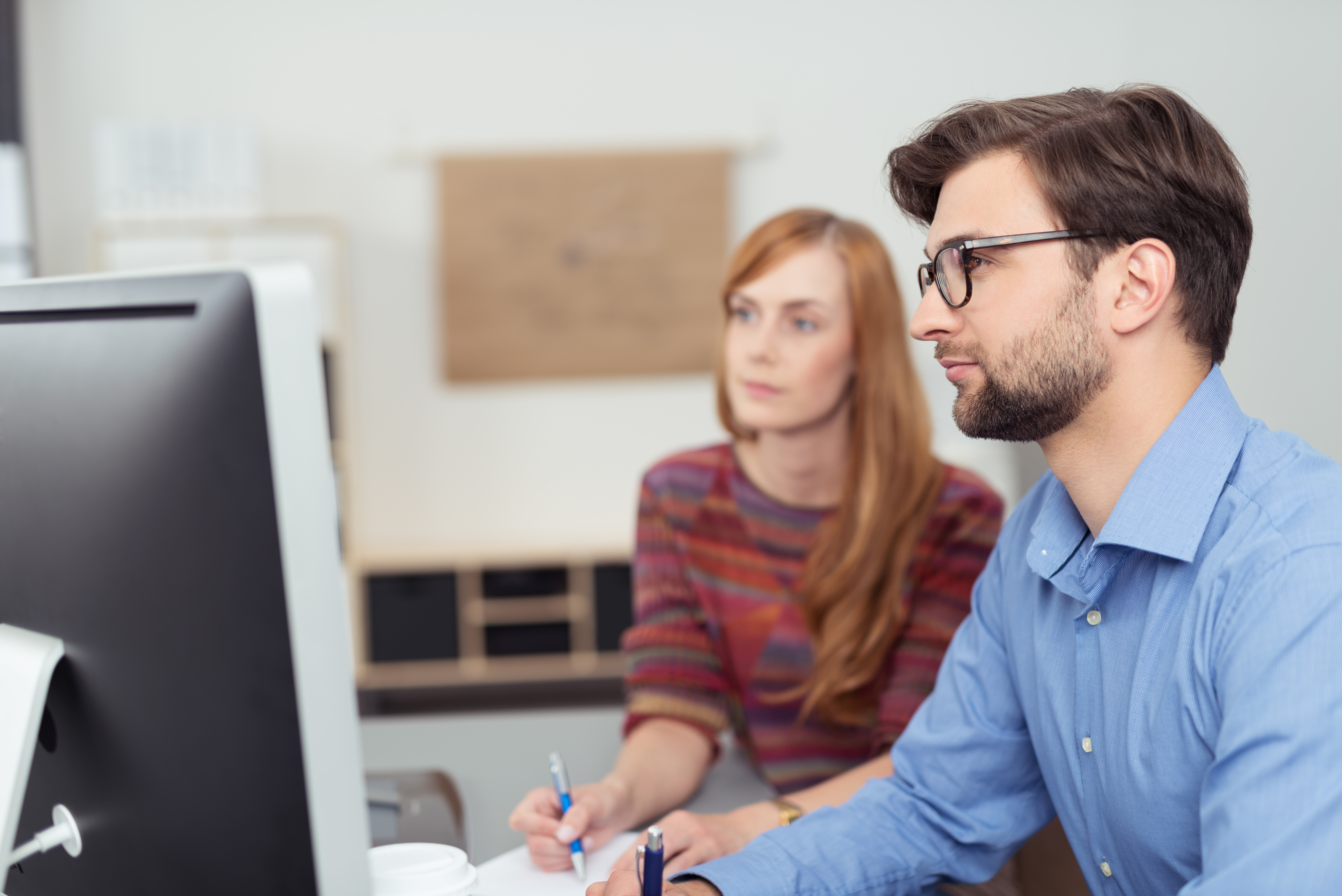 Junger bärtiger Mann und junge Frau sitzen vor einem Computer